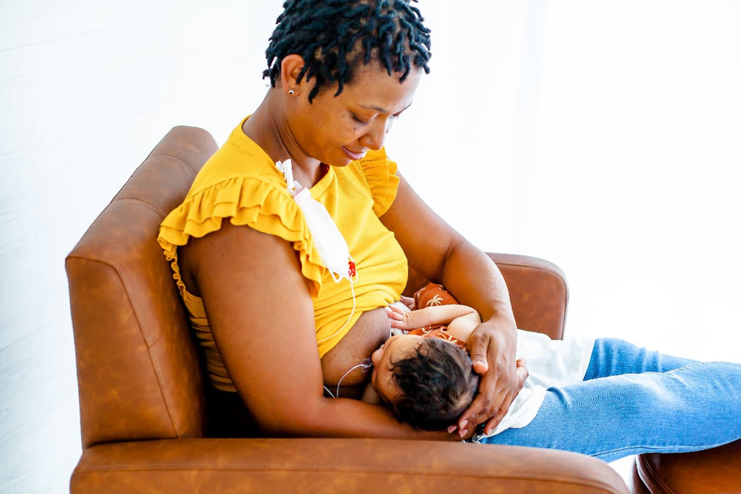 Parent using an at-breast supplemental feeding system to support breastfeeding